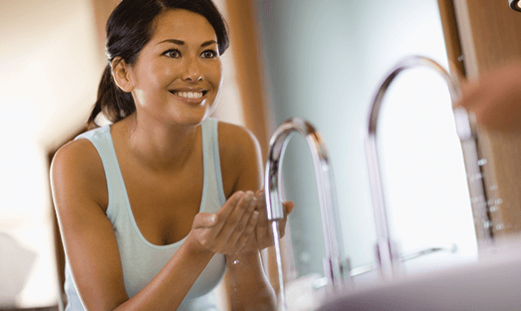 Woman looking in the mirror while cupping water from the sink in her hands