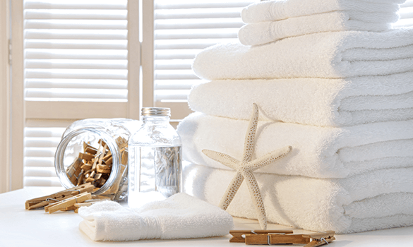 Six white towels stacked on top of each other with another folded towel next to a jar of clothespins