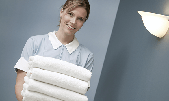 A smiling hotel maid holding four folded white towels