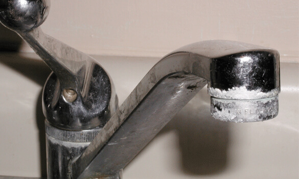 A sink faucet crusted with calcium buildup.