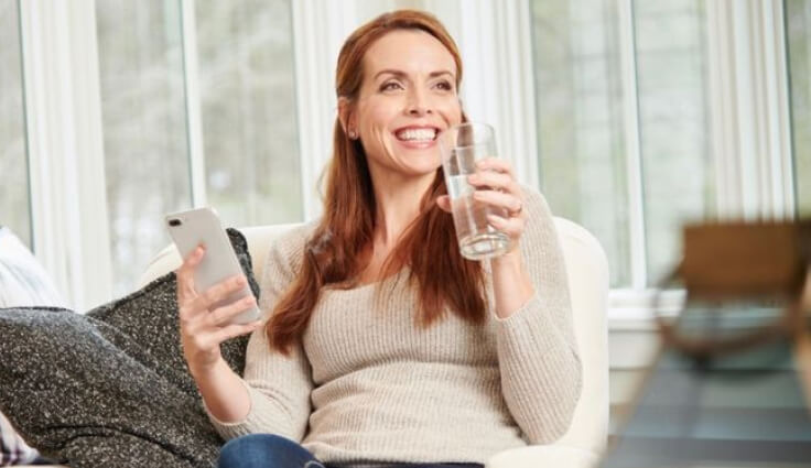 Woman smiling with phone in one hand, glass of water in the other