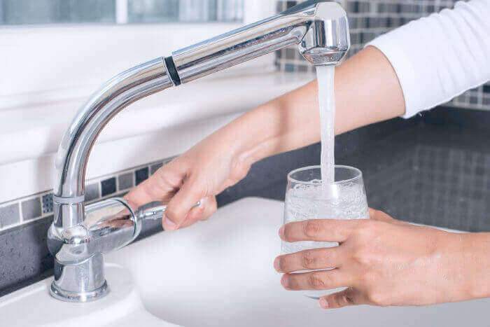 A person filling a cup of water at the kitchen sink.