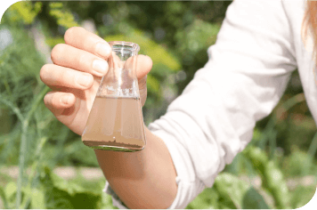 A hand holding a beaker of dirty water