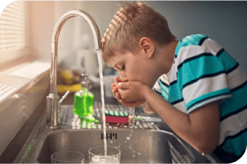 A boy drinking water out of a kitchen sink.