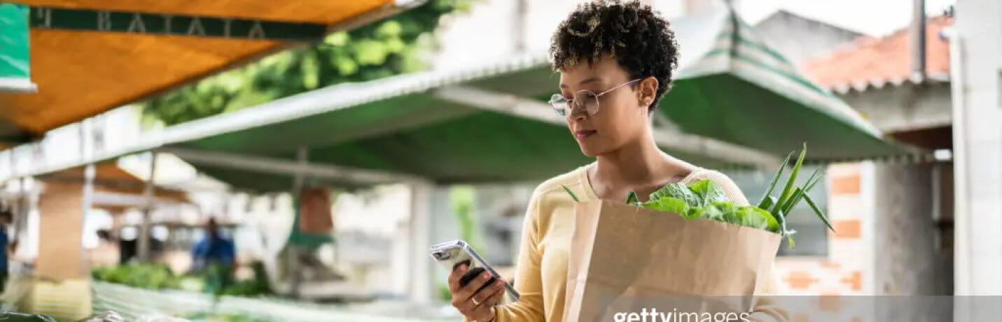 A woman looking at a phone holding a bag of groceries