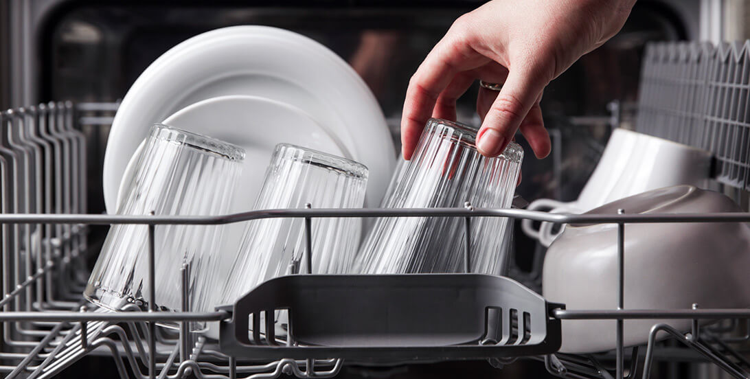 A hand putting a clear glass in the dishwasher