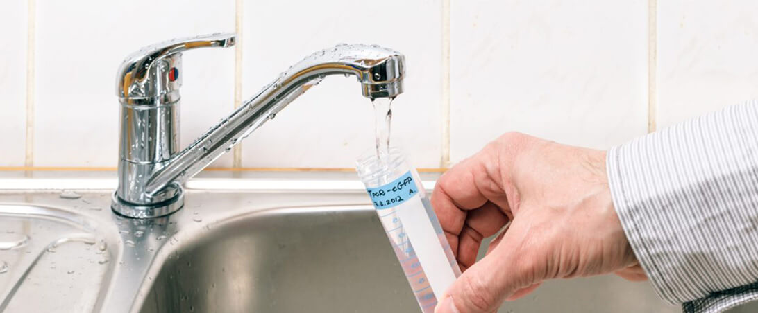 A close up of a mans hand holding a water test tube filling it with water.