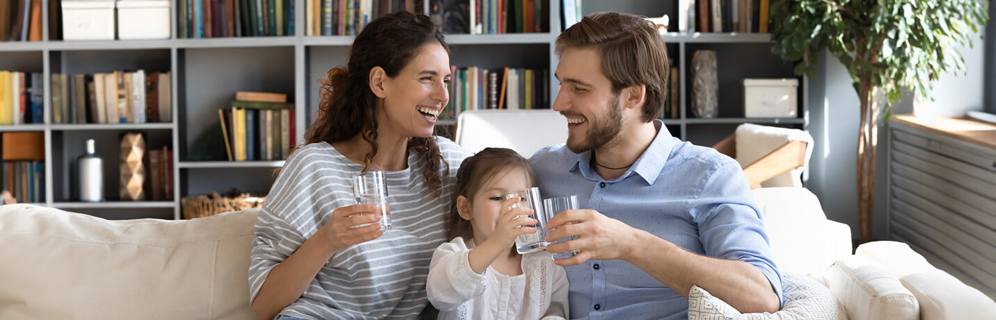 A man, woman, and young girl smiling with clear glasses of water.