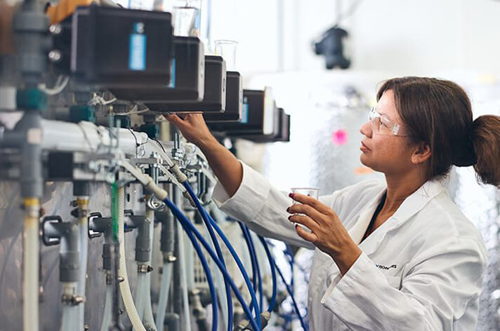 A woman with a lab coat and clear goggles looking at machinery.