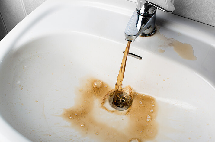 A sink with brown water running out of it.