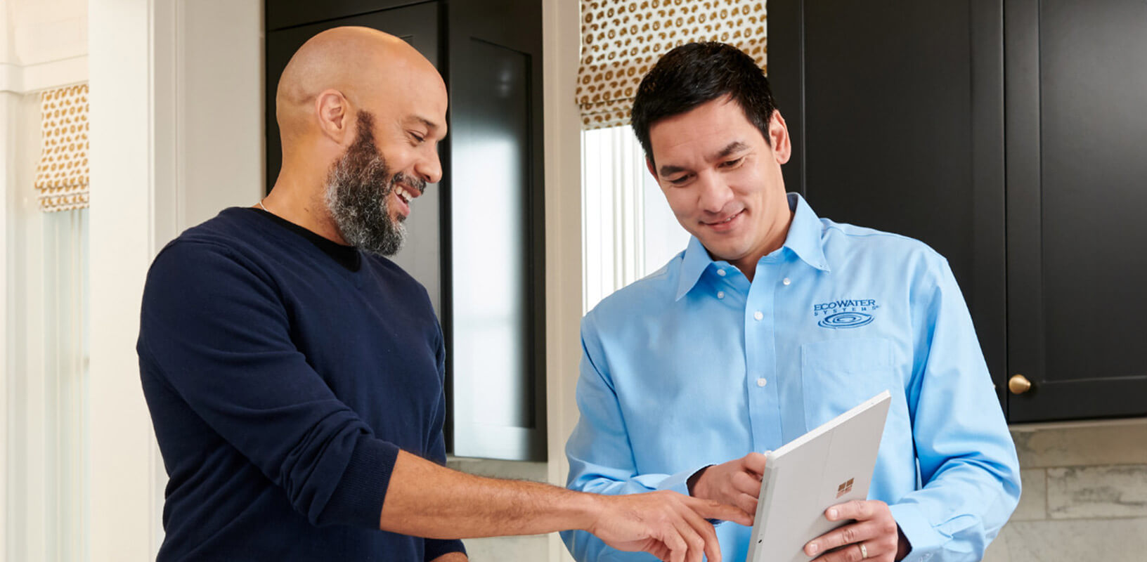 An EcoWater Dealer showing an ipad to a man in a kitchen.