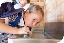 A girl drinking out of a water fountain at school.
