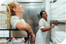 Two hospitality workers laughing in a room with white linens.