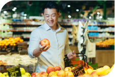 A man holding an apple in a grocery store.