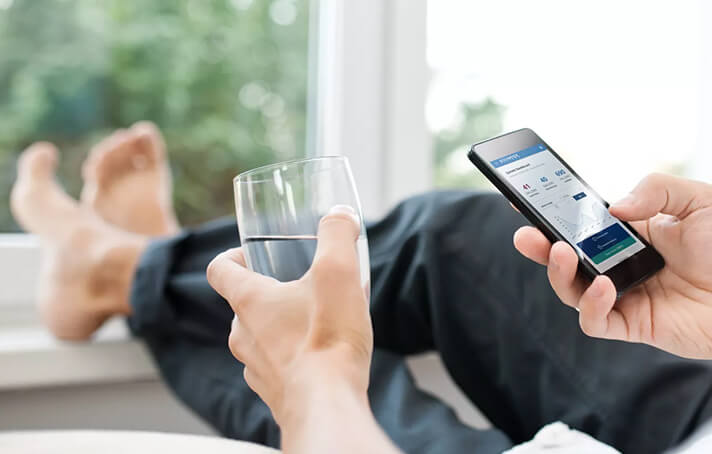 A person sitting with a clear glass of water in one hand and cell phone in the other.