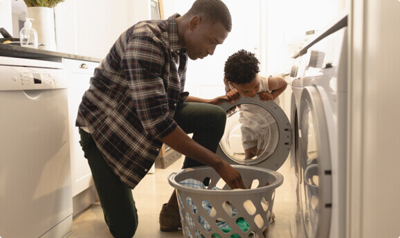 A man and young boy pulling laundry out of the dryer.