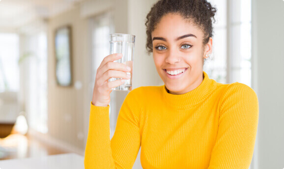A woman smiling holding a glass of water.