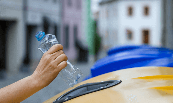 A hand placing a water in a recycling bin.