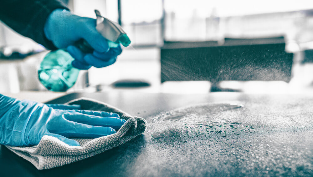 A person with rubber gloves spraying a surface.