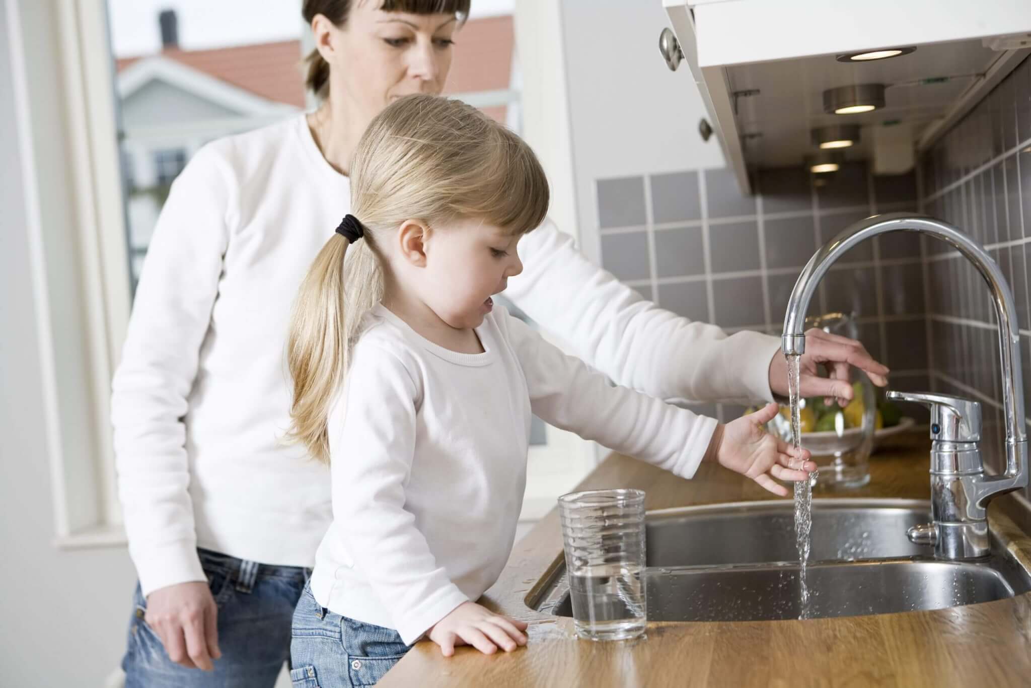 A woman and young girl at a kitchen sink.