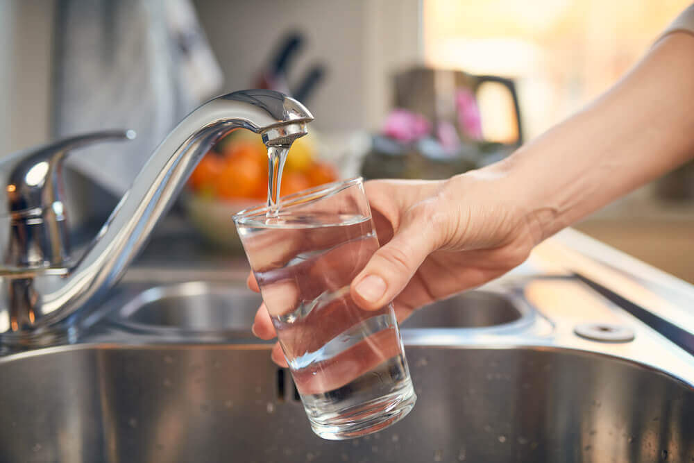 Une main remplissant un verre d’eau près de l’évier de la cuisine.