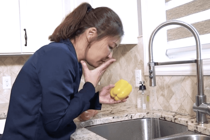 A woman holding a pepper, smelling her hand.