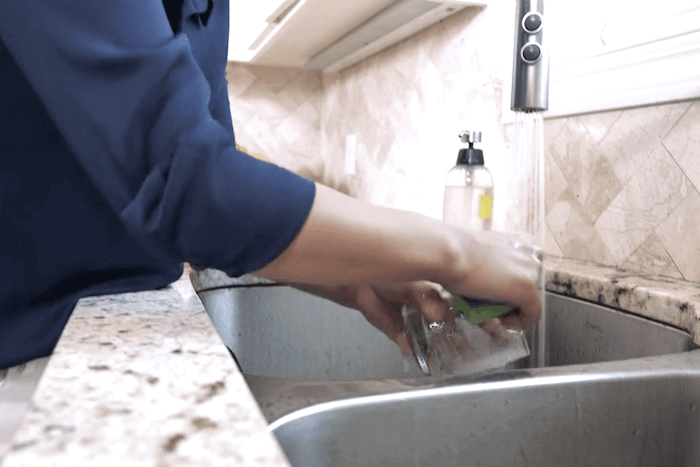 A person washing a drinking glass at a kitchen sink.