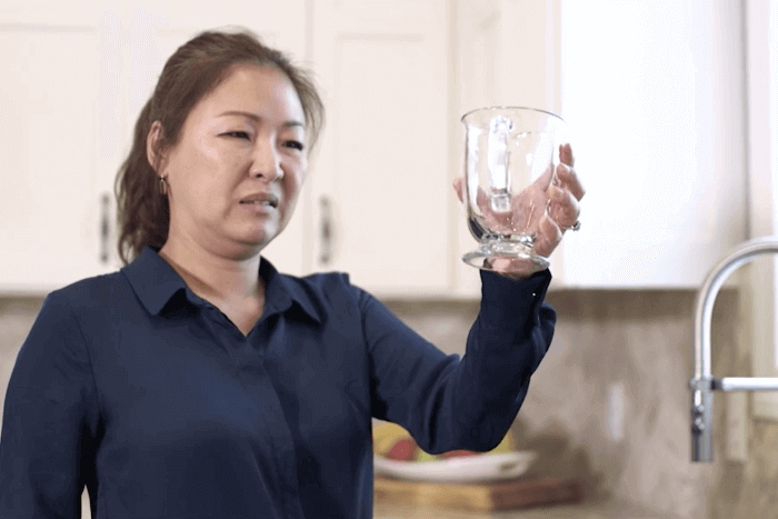 A woman looking at a glass that has water spots on it.